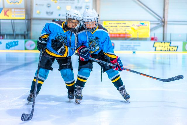 Two female ice hockey players in blue jerseys on a rink, engaged in a game.